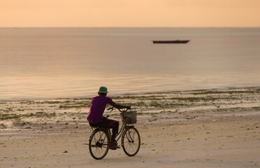 A man riding a bicycle on a Zanzibar beach at dawn in Tanzania - obrazy, fototapety, plakaty