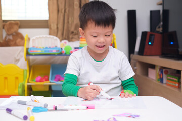 Cute happy smiling Asian 4 years old toddler boy child coloring with marker in living room at home, Creative play for toddler, improve focus in child concept