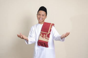 Portrait of attractive Asian muslim man in white shirt pulling hands towards camera, inviting someone to come inside, welcoming gesture. Isolated image on gray background