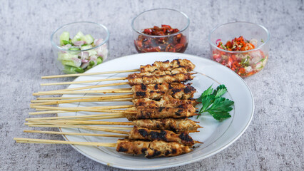 A plate of chicken satay served with celery, a glass of pickles, soy bean sauce and sambal matah in the room, their vibrant colors and aromas add to its delectable appeal. 