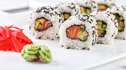Sushi with salmon on a white plate with wasabi, ginger, soy, chopsticks on a white background