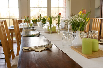 Large wooden table decorated for a dinner party with spring flowers, green candles and various...