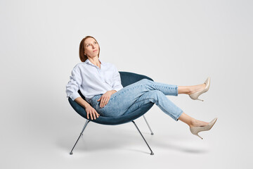 Carefree middle aged woman sitting in cosy armchair and waiving her legs
