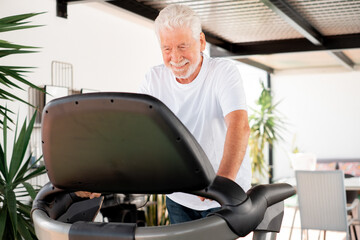 People sport concept. Happy senior man doing exercises to stay fit. Elderly bearded man in sportswear running on treadmill in home terrace