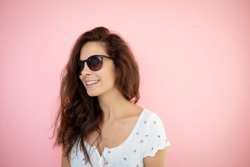 pretty young woman with black sunglasses and long hair with flowered shirt is standing in front of pink background
