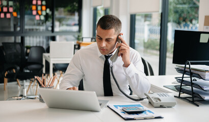 Businessman Talking on the phone and using a laptop with a smile while sitting at office