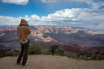 Young girl with sweatshirt and hoodie taking photos of the landscape of the Grand Canyon, her back is turned