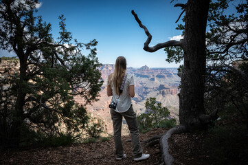 Young blonde girl with long loose hair standing in front of the landscape of the Grand Canyon, she carries a vintage photo camera on her back