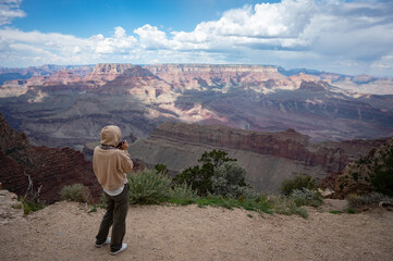 Young girl with sweatshirt and hoodie taking photos of the landscape of the Grand Canyon, her back...