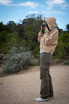 Vertical photo of a young girl in a sweatshirt and hoodie taking photos in nature