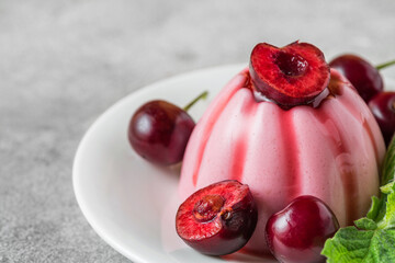 Italian cherry panna cotta dessert with fresh berries, syrup and mint leaf on gray background....