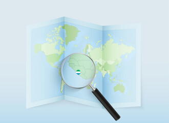 A folded world map with a magnifying lens pointing towards Sierra Leone. Map and flag of Italy in loupe.