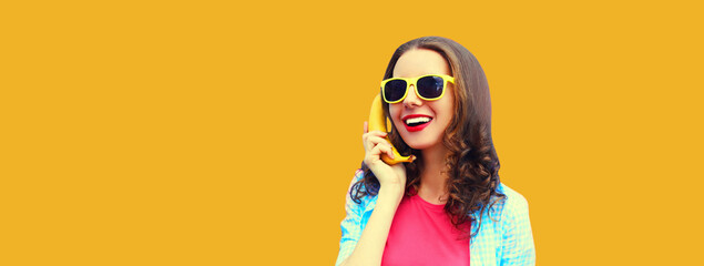 Portrait of funny young woman calling on banana phone looking away on orange background - Powered by Adobe