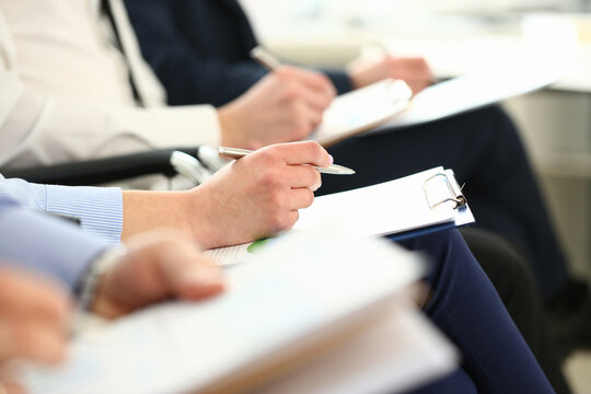 Businessmen are holding documents while taking notes at seminar