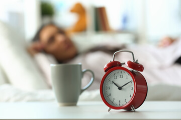 Red alarm clock at ten o'clock and sleeping woman