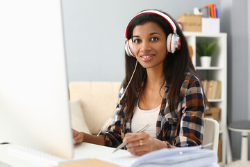 African female student wears headphones studying alone at home office desk