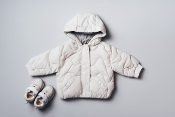 Puffer jacket and boots on grey background. Set of baby clothes for winter. Newborn fashion kids outfit. Top view, flat lay. Copy space © jchizhe
