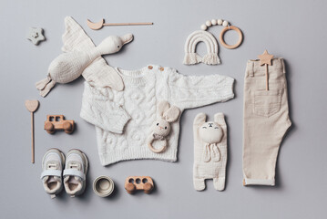 Set of baby stuff and accessories for newborn on brown background. Baby shower or baby care concept. Flat lay, top view. Knitted sweater, pants, shoes, bib, wooden toys and soft bird.