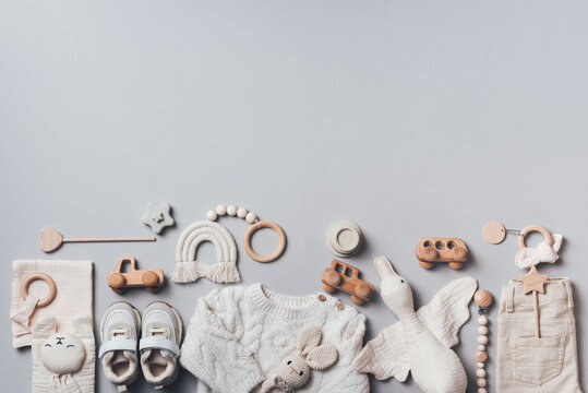 Set of baby stuff and accessories for newborn on brown background. Baby shower or baby care concept. Flat lay, top view. Knitted sweater, pants, shoes, bib, wooden toys and soft bird.