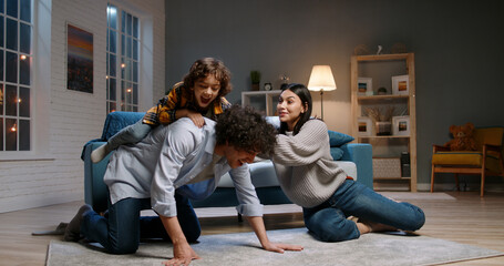 Funny asian family relaxing at home together. Little kid with curly hair jumping onto his father, doing a piggy back ride and laughing - happy family, recreational pursuit 