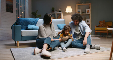 Cute young asian family spending time together at home. Little boy with curly hair reading a book with his parents, happily smiling - happy family, recreational pursuit concept