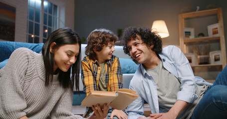 Happy young asian family having fun together. Little boy with curly hair reading a book with his...