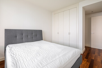 Double bed with wooden laminate floor and white walls and with built-in wardrobe on a sunny summer day. Concept of motel room or a bedroom after renovation. Copyspace