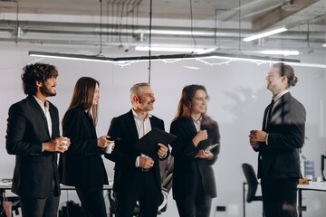 Obraz premium Smiling office workers talking during coffee break. Ambitious business people discussing new ideas. Company executive and his employees having fun