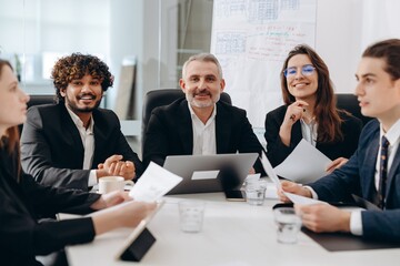 Smiling team of investors sitting at a table in an office space. Business partners sitting in the office discussing new startups.