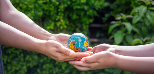 Close-up of a woman's hand giving an asteroid world to a boy on a blurry green background.hands holding planet earth save the earth.
