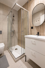 Diagonal shot of small bathroom with stylish white vanity glass shower and ceramic sink with beautiful beige tiles. Concept bathroom after renovation in the apartment