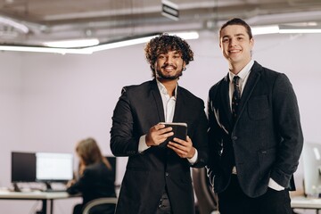 Two young businessmen with digital device. Indoor shot of smiling office managers with tablet