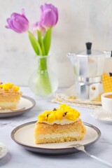 Sliced biscuit cake with cream cheese cream, lemon layer and yellow biscuit decor on a ceramic plate on a light background. Recipes for biscuit cakes.