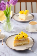Sliced biscuit cake with cream cheese cream, lemon layer and yellow biscuit decor on a ceramic plate on a light background. Recipes for biscuit cakes.