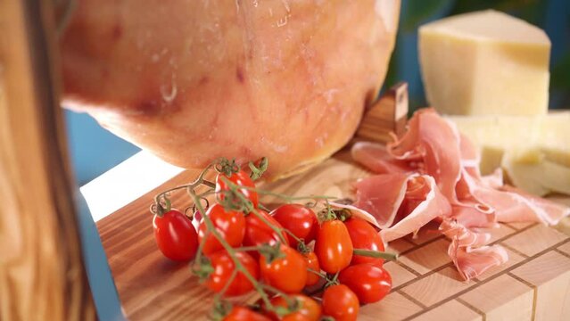 Salted parma ham leg on wooden stand with cut slices, tomatoes and red wine, traditional mediterranean antipasto food, selection of high quality cured ham for luxury catering service, dry cured jamon
