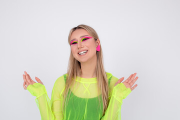 Happy young model laughs in studio on light background, demonstrates fashionable neon makeup, spreading her palms.