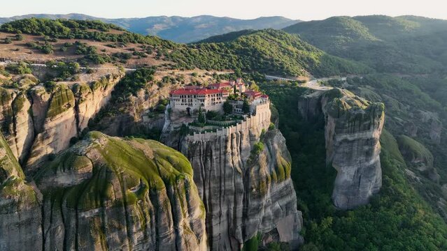 Flying over Meteora Monasteries at sunrise, Greece. Landscape scenery with green hills, rocks, and old Monasteries on it. Aerial view, 4K