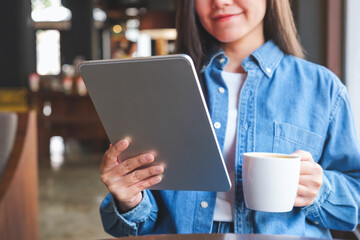 Closeup of a young woman holding and using digital tablet while drinking coffee in cafe
