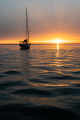 sailboat sailing in the sea to the left of the sunset. vertical photo with copy space.