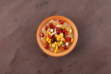 Noah's pudding or Noah's Dessert. Ashure or Asura Dessert, also called as Anusabur in clay bowl on brown background, top view. Turkish delicious porridge with grains, fruits, and nuts