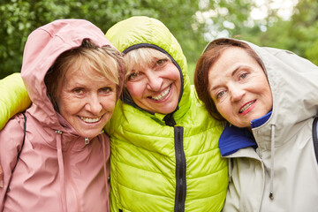 Smiling elderly female friends in jackets exploring forest