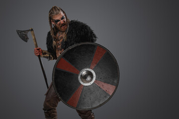 Studio shot of redhead scandinavian warrior from past with shield and hatchet.
