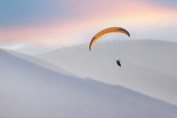 A paraglider is planning in the sky in a hilly area.