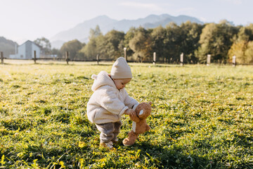 Child playing outdoors with a plush teddy bear, dancing with it, on a cold spring morning, on...