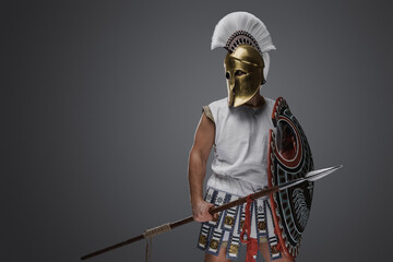 Studio shot of isolated on gray background soldier from ancient greece with shield and spear.