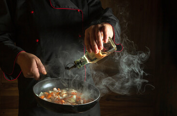 The chef adds oil to a steaming hot pan. The idea of European cuisine for a hotel with advertising...