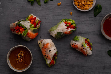 Summer rolls with fresh vegetables and shrimps or prawns and peanut and chili sauce on dark grey background. Vietnamese appetizer. Top view. Healthy food concept
