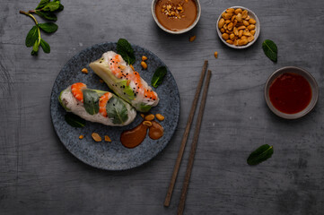 Summer rolls with fresh vegetables and shrimps or prawns and peanut and chili sauce on dark grey background. Vietnamese appetizer. Top view. Healthy food concept