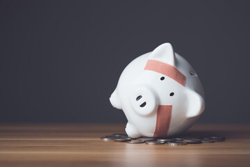 Plakat Financial problem, Bankrupt or fail in business concept. White piggy bank with plastic adhesive bandages on wooden desk with dark copy space wall background. Fail, Bankrupt or unsuccessful idea.