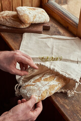 Close up male hands with ciabatta bread and linen bag. Wooden background with window. Organic and healthy concept. Top view